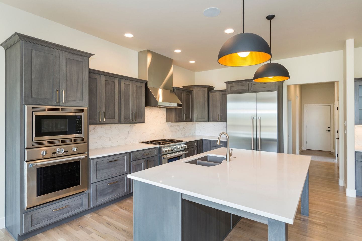 Modern kitchen with grey cabinetry, stainless steel appliances, a large island with a built-in sink, and two pendant lights hanging from the ceiling—an ideal space for any home decor enthusiast.