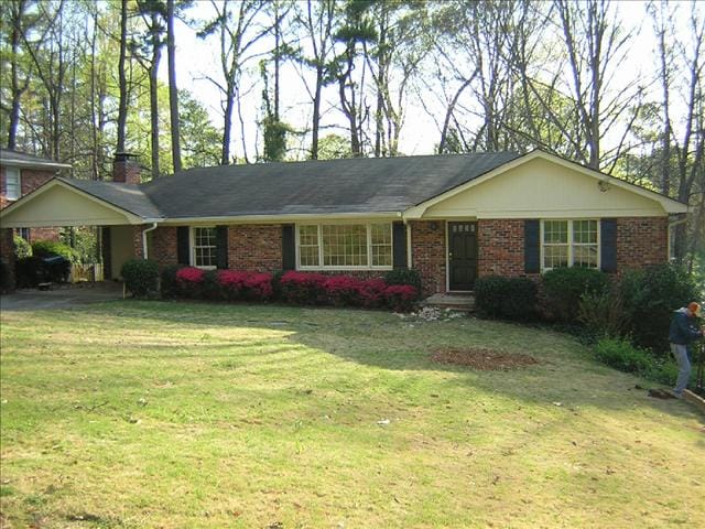 Single-story brick house with a gable roof, front porch, and large windows. Front yard with trimmed bushes, red azaleas, and a sloping lawn. A person is seen near the right edge of the image, possibly planning home expansions to enhance their charming residence.