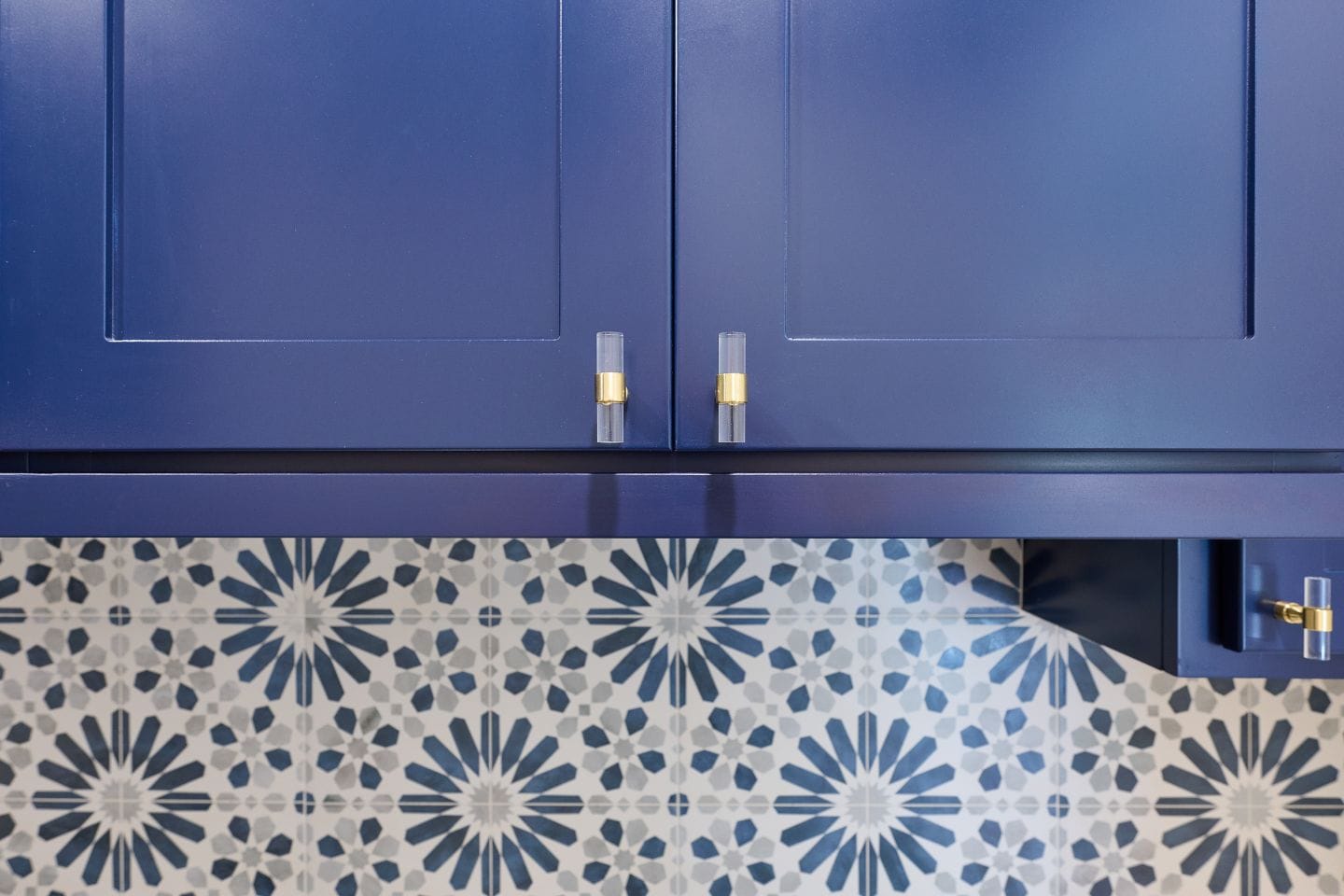 Blue kitchen cabinets with golden handles above a tiled backsplash featuring a blue and white geometric pattern, perfect for your next kitchen remodeling project.