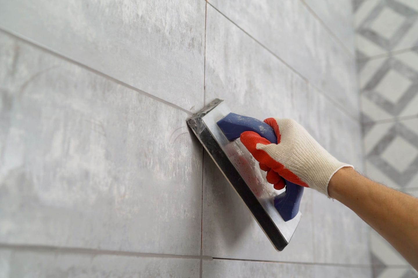 A gloved hand using a grout float to apply grout to wall tiles, perfecting the tiling for a seamless finish.