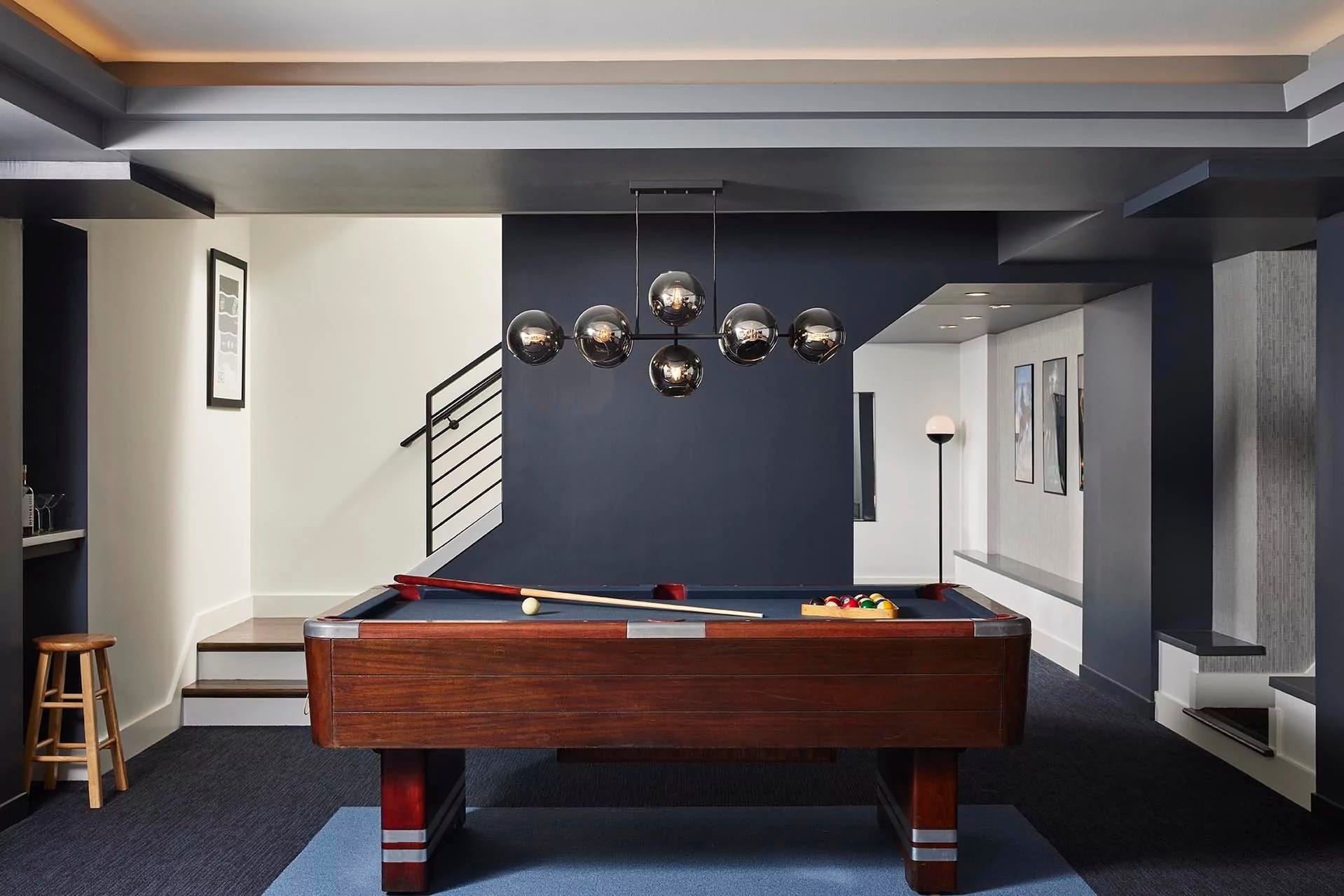 A well-lit room with a pool table centered below spherical pendant lights, surrounded by modern decor and artwork—an ideal example of basement remodeling.